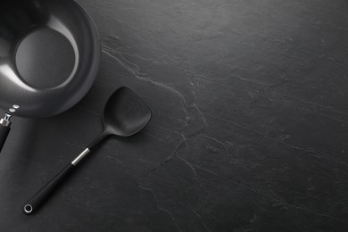 Photo of Black metal wok and spatula on dark textured table, top view. Space for text