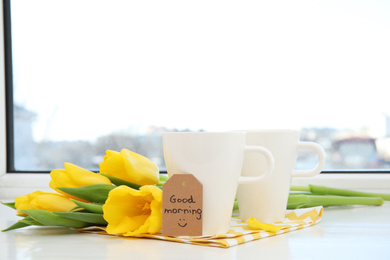 Photo of Aromatic coffee, beautiful flowers and GOOD MORNING wish on light windowsill