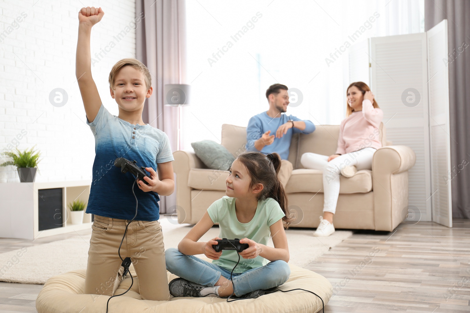 Photo of Cute children playing video games while parents resting on sofa at home