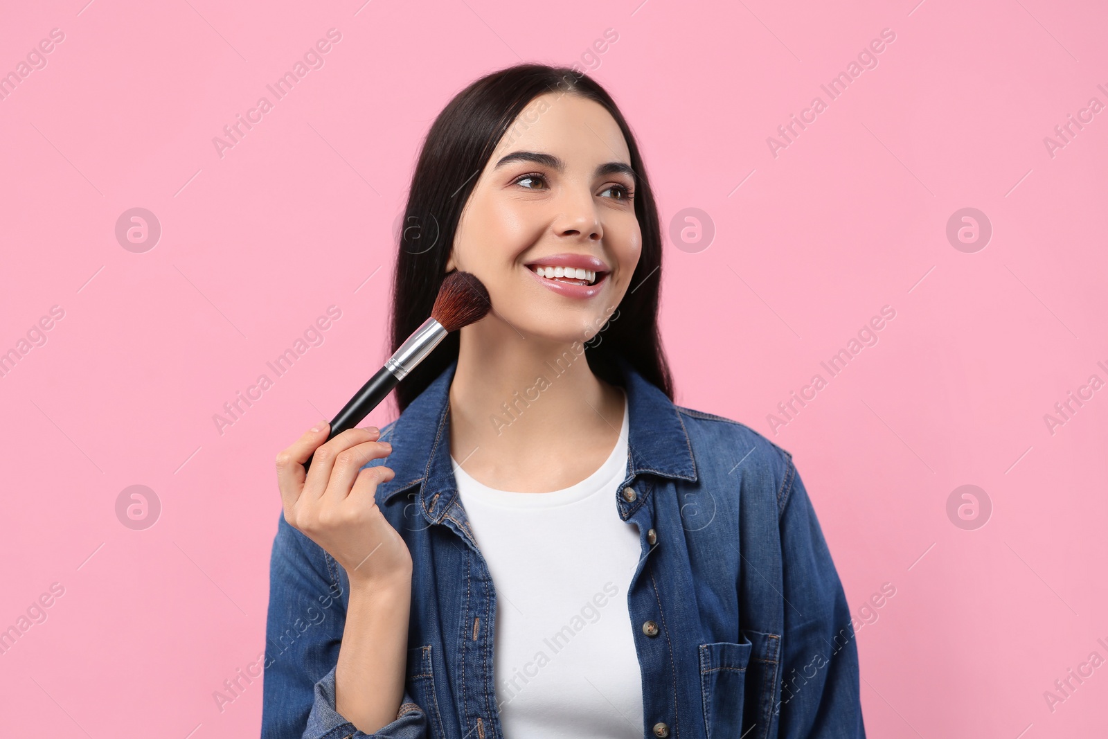 Photo of Beautiful woman applying makeup with brush on pink background