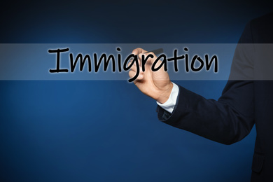Image of Businessman writing word IMMIGRATION on virtual screen against blue background, closeup