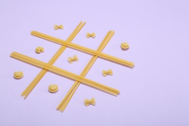 Photo of Tic tac toe game made with different types of pasta on lilac background