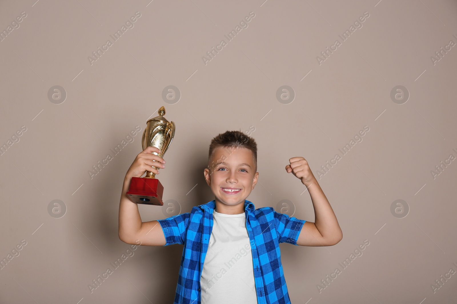 Photo of Happy boy with golden winning cup on beige background