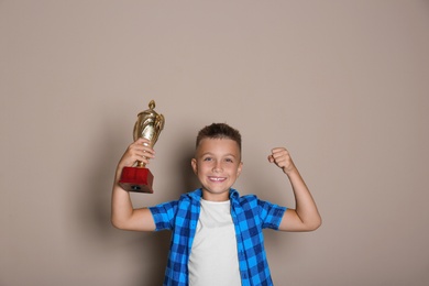 Happy boy with golden winning cup on beige background