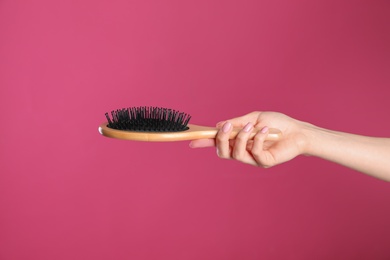 Photo of Woman holding wooden hair brush against crimson background, closeup