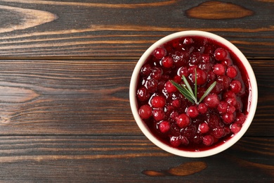 Photo of Fresh cranberry sauce with rosemary on wooden table, top view. Space for text