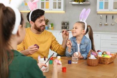 Happy family having fun while painting Easter eggs at table in kitchen