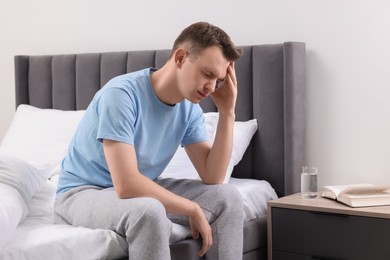 Photo of Sad man suffering from headache on bed indoors, space for text