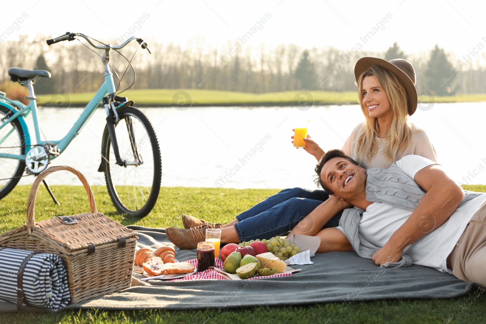 Photo of Happy young couple having picnic near lake on sunny day