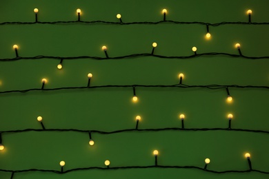 Glowing Christmas lights on green background, top view