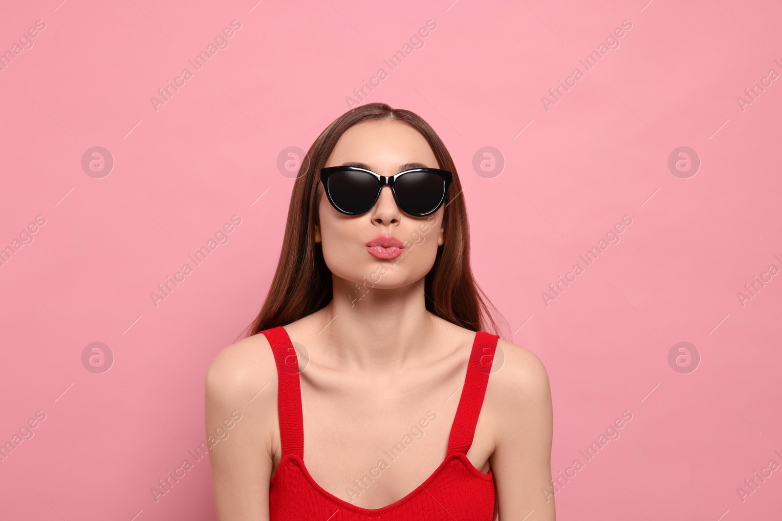 Photo of Beautiful young woman with sunglasses blowing kiss on pink background