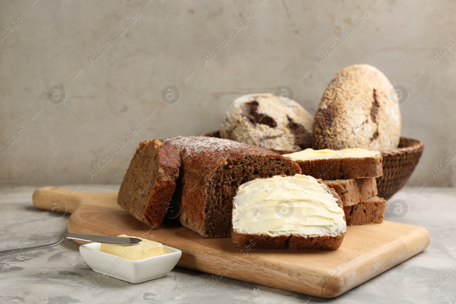 Photo of Tasty freshly baked bread with butter on grey table