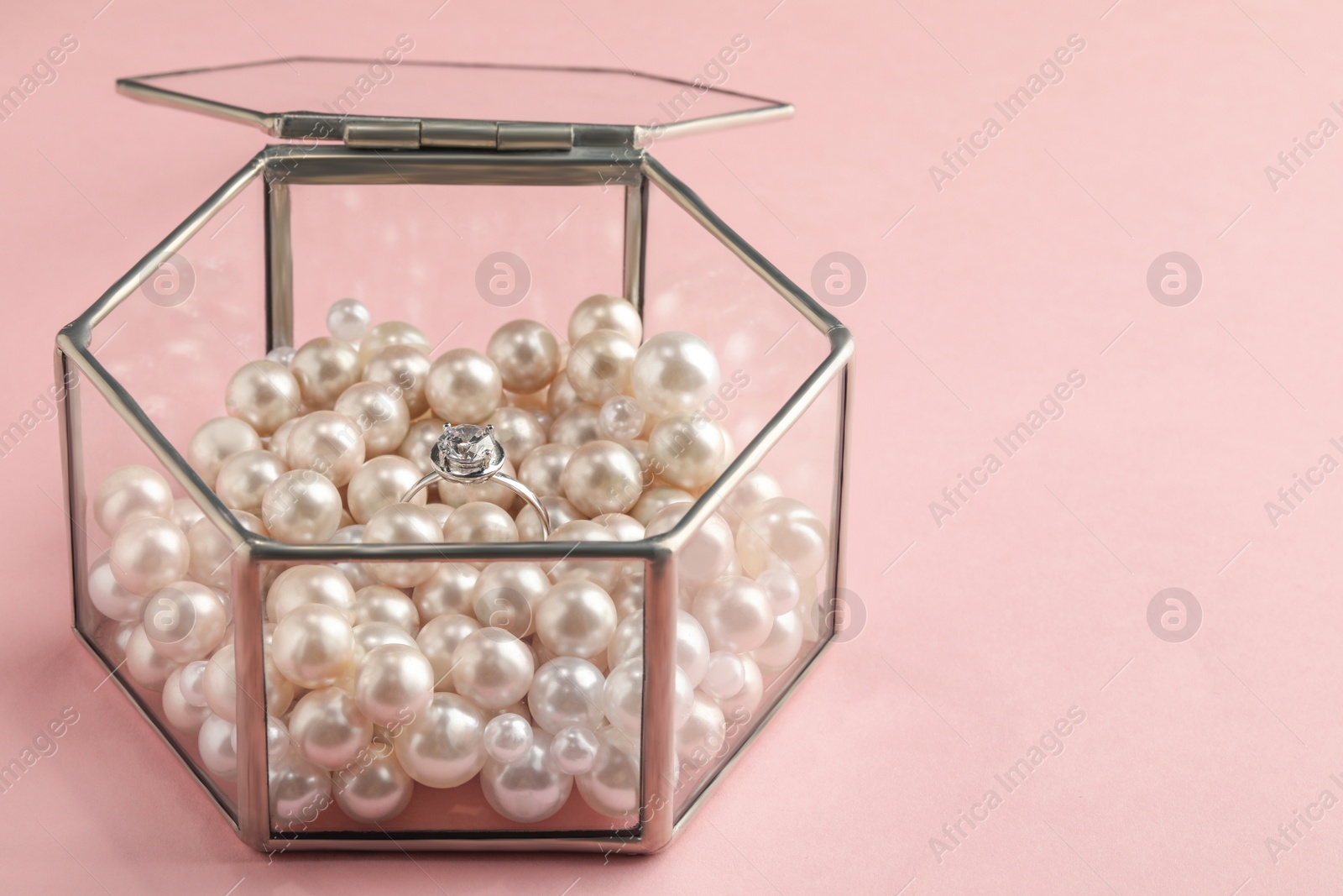 Photo of Glass box with decor pearls and engagement ring on pink background, space for text