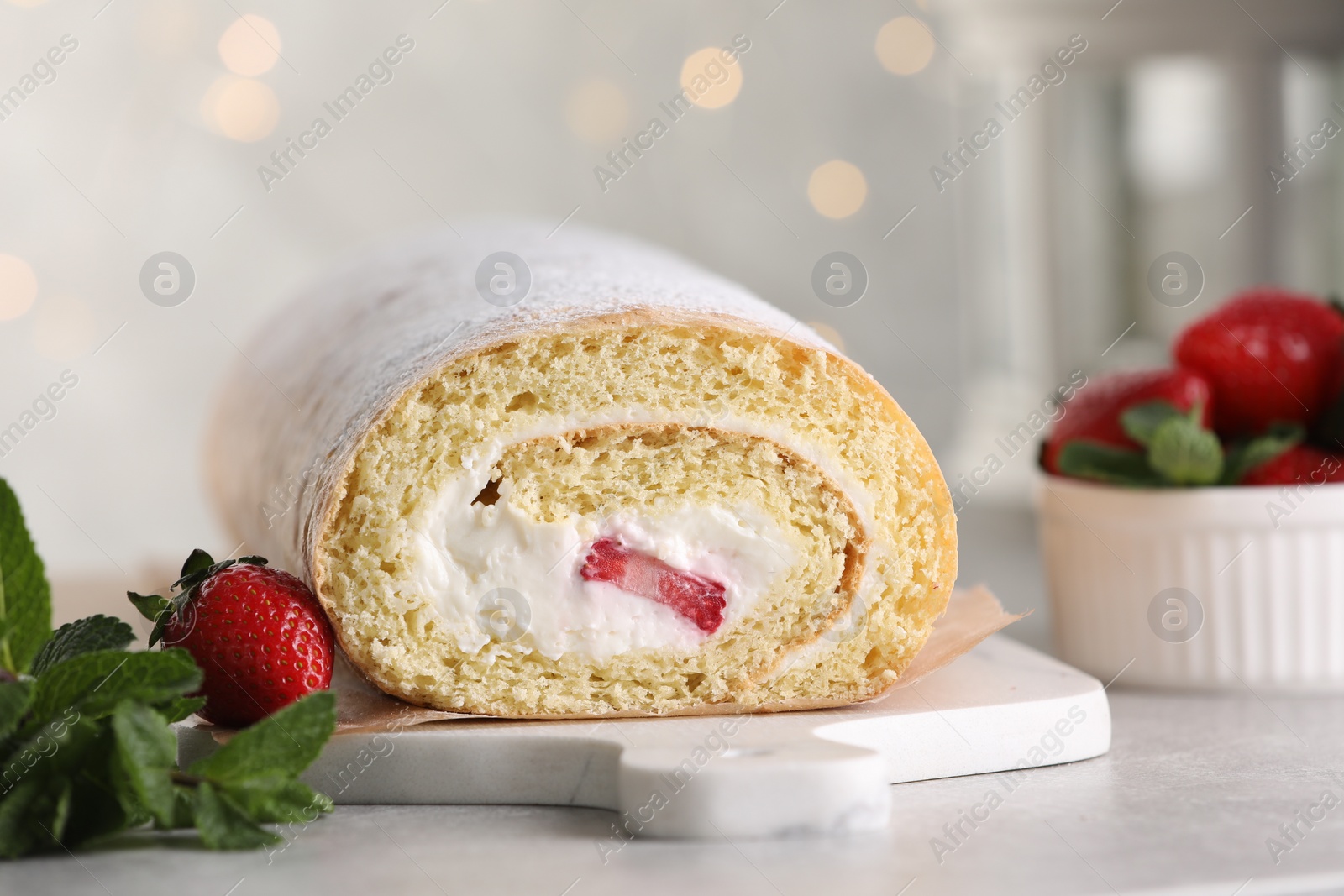 Photo of Delicious sponge cake roll with strawberries and cream on light grey table against blurred lights, closeup