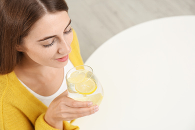 Young woman drinking lemon water at white table, above view. Space for text