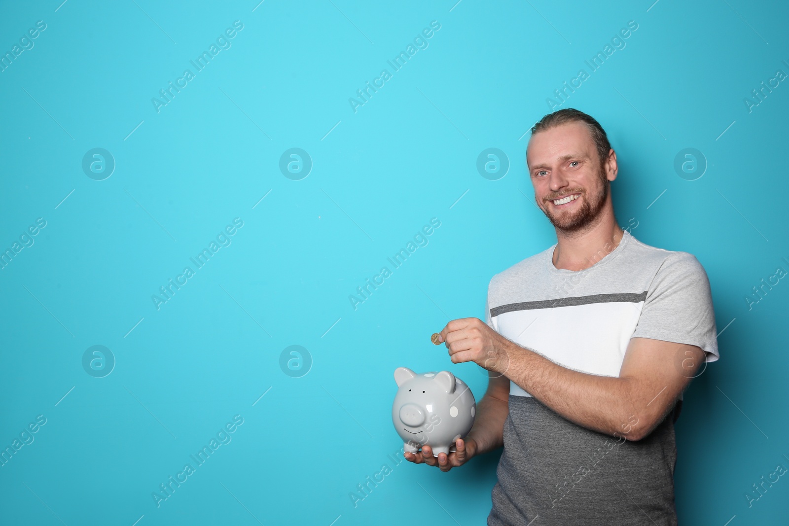 Photo of Happy man putting coin into piggy bank on color background. Space for text