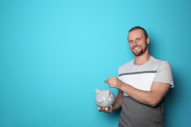 Happy man putting coin into piggy bank on color background. Space for text