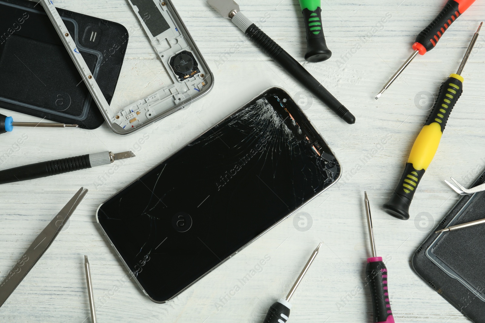 Photo of Damaged smartphone and repair tools on white wooden background, flat lay