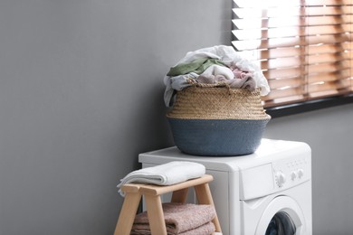 Photo of Wicker basket with dirty laundry on washing machine near grey wall indoors