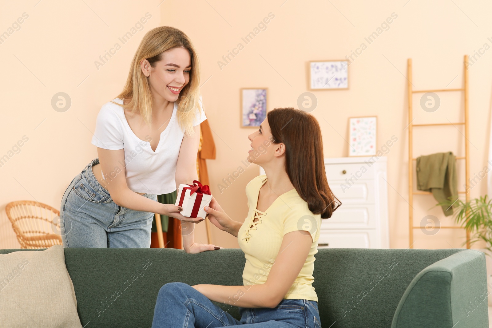 Photo of Smiling young woman presenting gift to her friend at home