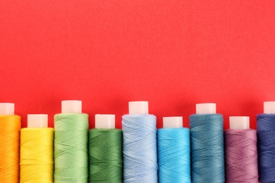 Photo of Different colorful sewing threads on red background, flat lay. Space for text