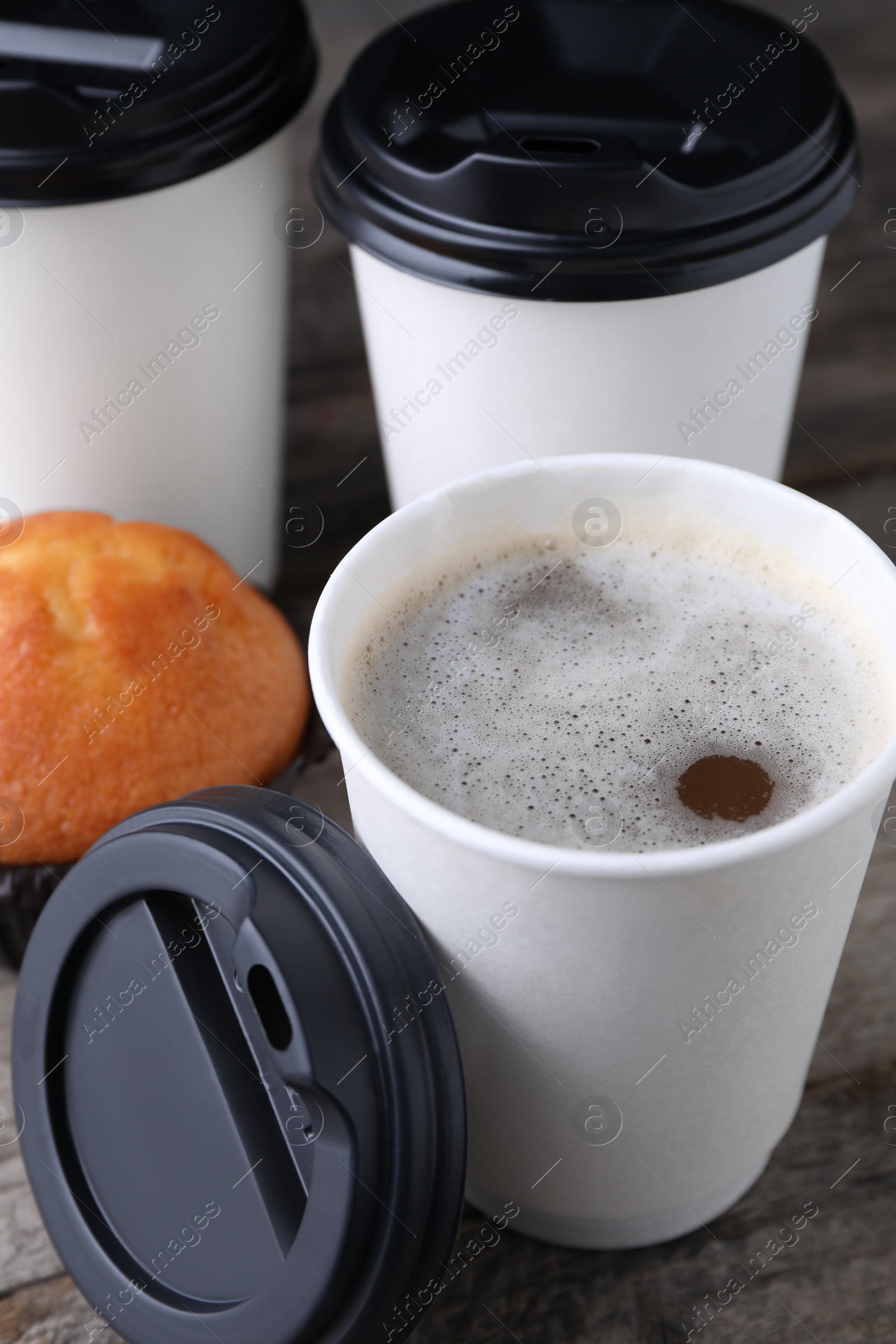 Photo of Coffee to go. Paper cups with tasty drink and muffin on table, closeup