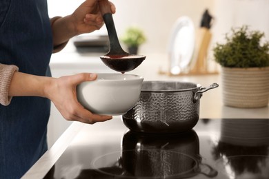 Photo of Woman pouring tasty soup into bowl at countertop in kitchen, closeup