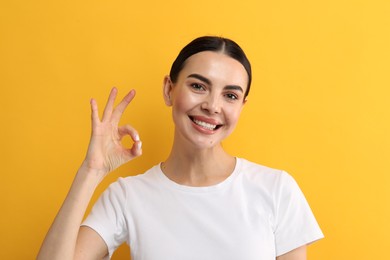 Beautiful woman with clean teeth smiling and showing OK gesture on yellow background