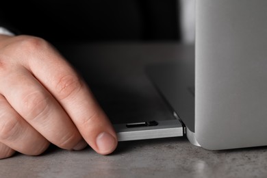 Photo of Man connecting usb flash drive to laptop at grey table, closeup