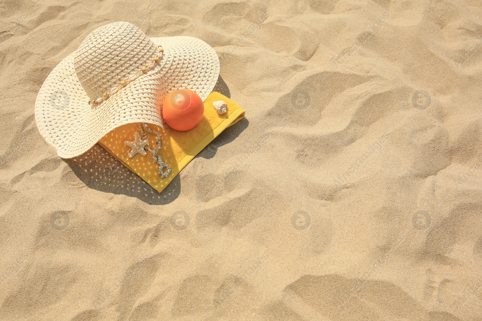 Photo of Straw hat, towel and orange on sand, above view. Space for text