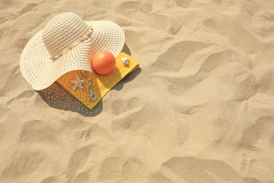 Straw hat, towel and orange on sand, above view. Space for text