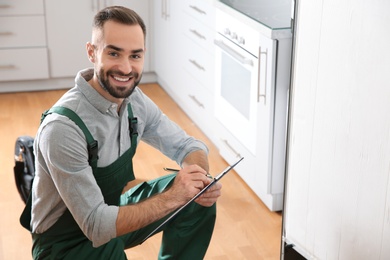 Photo of Male technician with clipboard examining refrigerator in kitchen