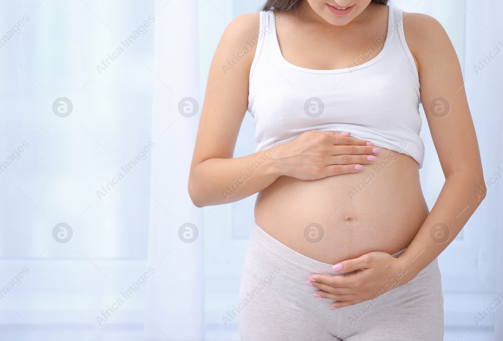 Photo of Young pregnant woman near window at home, closeup