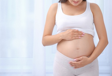 Young pregnant woman near window at home, closeup