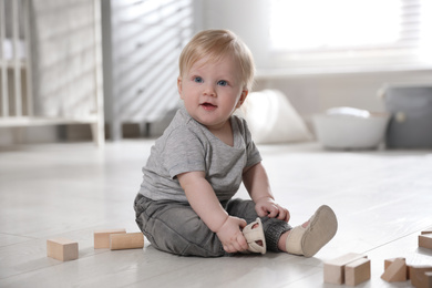 Photo of Adorable little baby with wooden blocks on floor at home