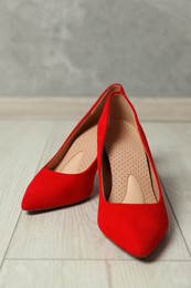 Photo of Orthopedic insoles in high heel shoes on floor, closeup