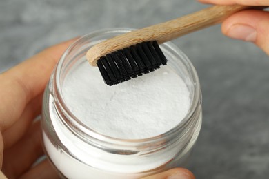 Photo of Young woman with toothbrush and jar of baking soda at grey table, closeup
