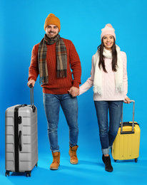 Photo of Happy young couple in warm clothes with suitcases on blue background. Winter vacation