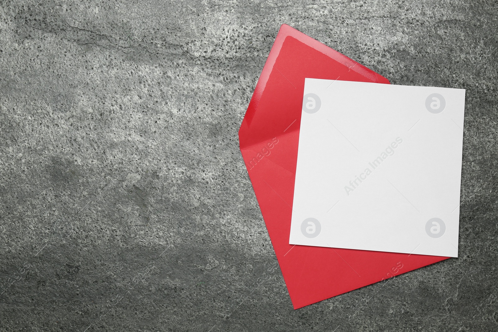 Photo of Envelope with blank paper card on grey table, top view. Space for text