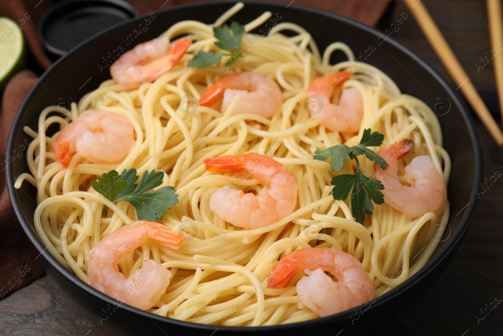 Photo of Tasty spaghetti with shrimps and parsley in bowl on wooden table, closeup