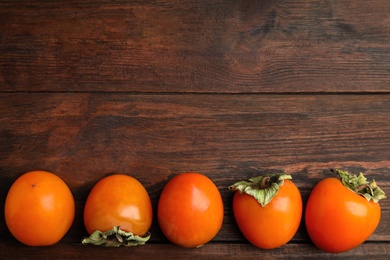 Photo of Delicious fresh persimmons on wooden table, flat lay. Space for text