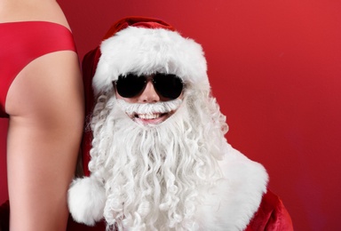 Photo of Young Santa Claus with sexy naked woman on color background
