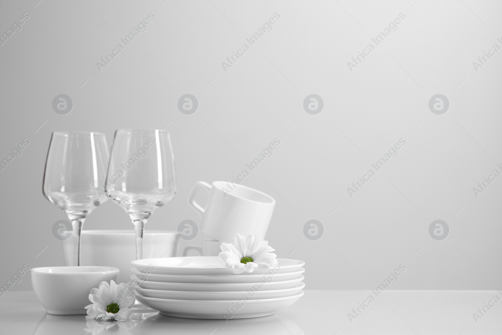 Photo of Set of many clean dishware, flowers and glasses on light table. Space for text