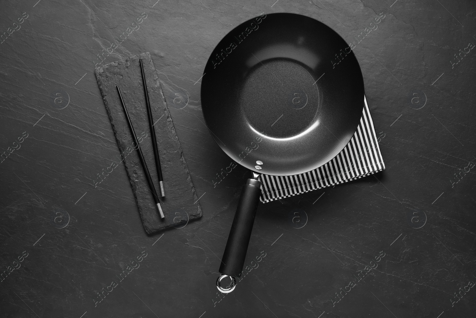 Photo of Empty iron wok and chopsticks on black table, flat lay