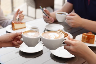 Photo of Friends drinking coffee at wooden table in outdoor cafe, closeup