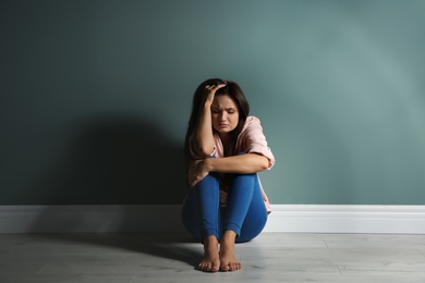 Photo of Depressed young woman on floor near color wall