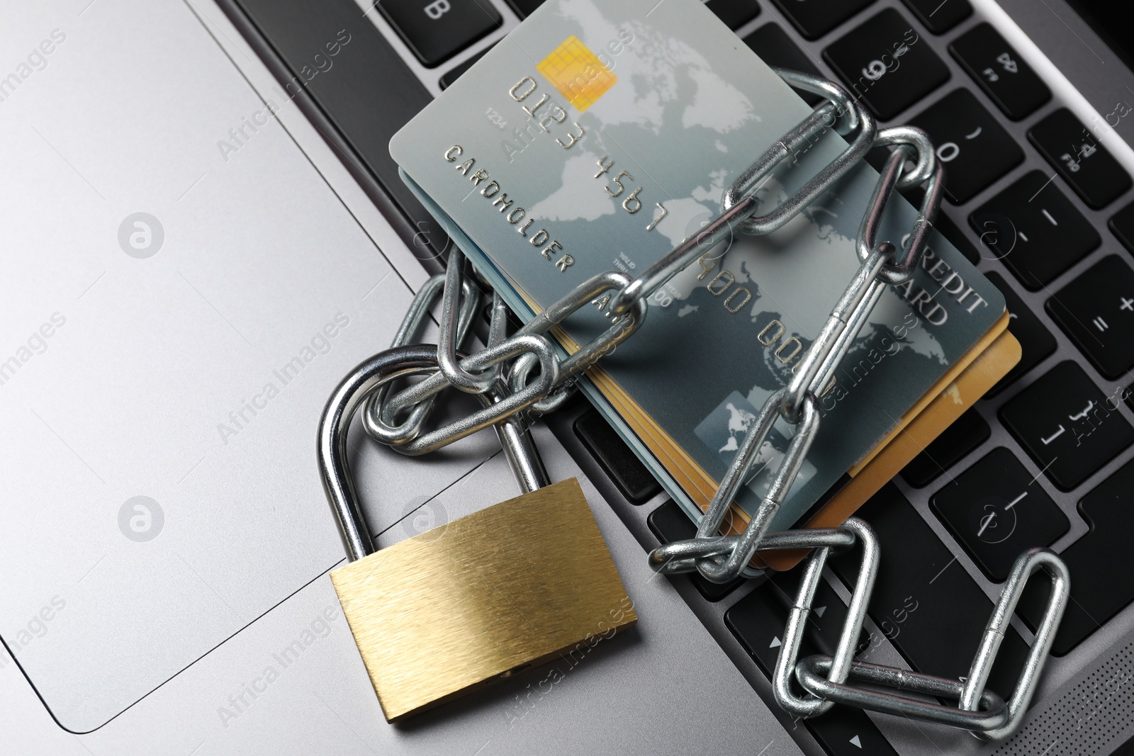 Photo of Cyber security. Metal padlock with chain and credit cards on laptop, top view