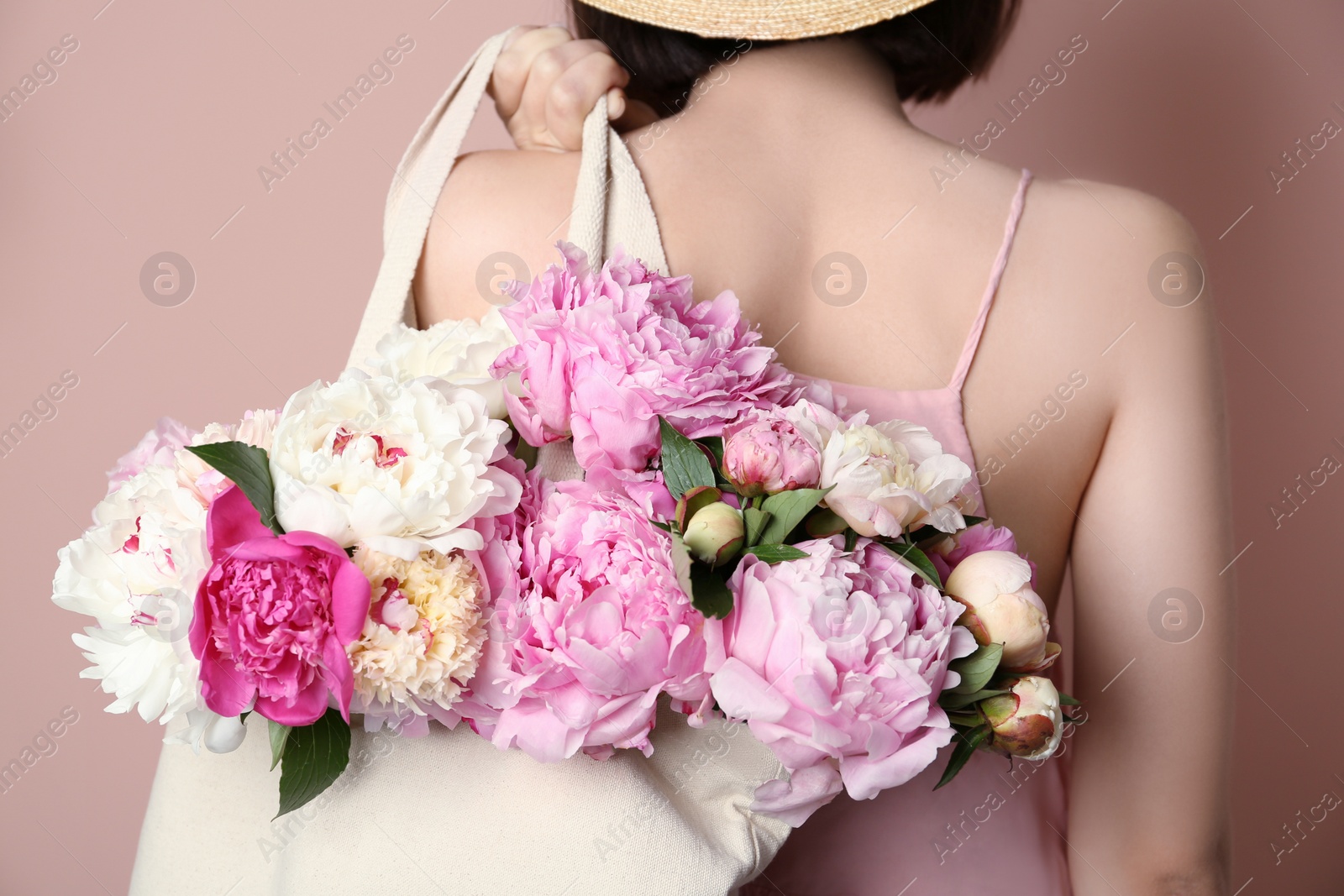 Photo of Woman with bouquet of beautiful peonies in bag on beige background, closeup