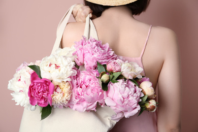 Woman with bouquet of beautiful peonies in bag on beige background, closeup