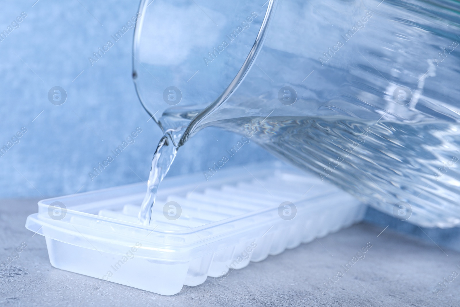 Photo of Pouring water into ice cube tray on light grey table, closeup